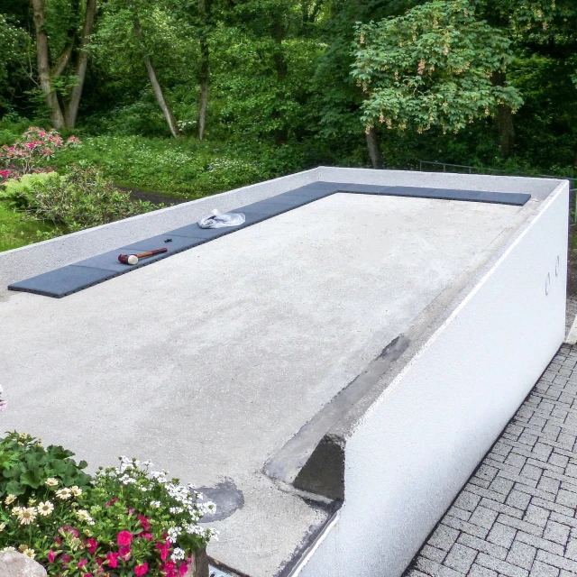 Auf dem Betondach einer Garage, die neben einem Wohnhaus am Hang steht, wird eine Dachterrasse gebaut. Dazu legt der Hausbesitzer schiefergraue Terrassenplatten von WARCO einfach auf das vorhandene, ebene Garagendach auf.