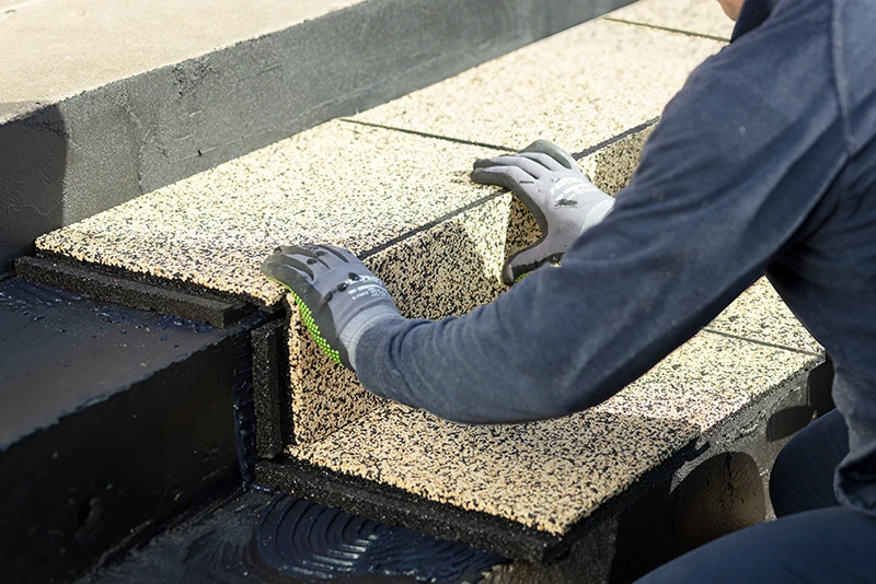 Mann klebt Treppenstufen fest. Gelber Treppenbelag wird verklebt auf der Trittfläche, sowie auf der Stoßstufe.