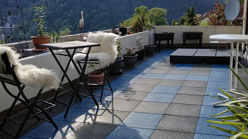 Großzügige Dachterrasse mit blau-grauem Plattenmuster, dekorativen Pflanzkübeln und gemütlicher Sitzgruppe: WARCO Terrassenplatten Classic verbinden wohnliches Ambiente mit trittsicherem Komfort und laden zum Entspannen im Freien ein.