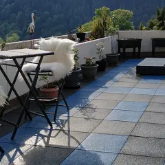 Großzügige Dachterrasse mit blau-grauem Plattenmuster, dekorativen Pflanzkübeln und gemütlicher Sitzgruppe: WARCO Terrassenplatten Classic verbinden wohnliches Ambiente mit trittsicherem Komfort und laden zum Entspannen im Freien ein.