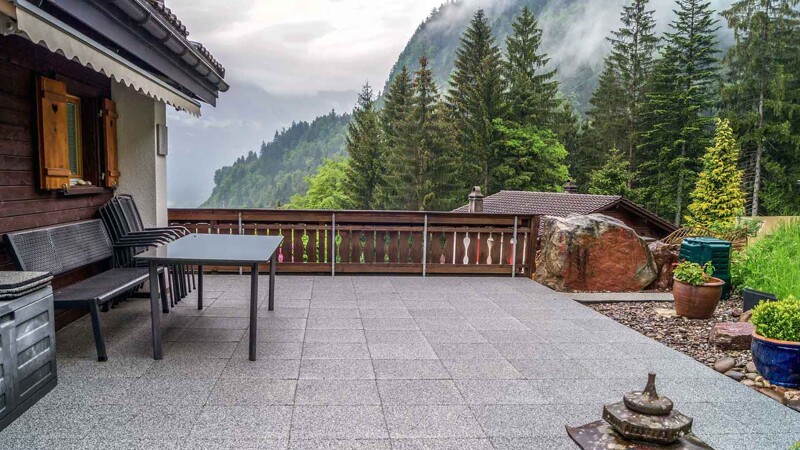 Vor dem Hintergrund der Schweizer Alpen ist ein Chalet mit großzügig angelegter Terrasse in den Hang gebaut. Die Terrasse selbst ist mit quadratischen Terrassenplatten von WARCO im Farbdesign heller Granit belegt.