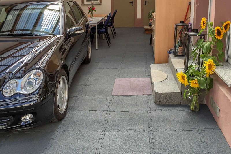 Eine schwarze Mercedes Limousine steht vor dem Eingang zum Haus in einem für Rheinhessen oder die Pfalz typischen Winzerhof. Die Hoffläche ist mit grauen Gehwegplatten aus Gummigranulat von WARCO ausgelegt.