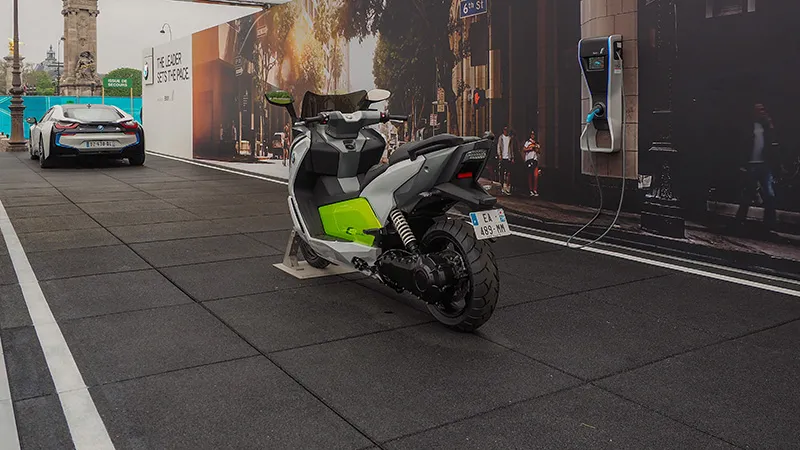 Elektroroller und E-Auto auf stoßdämpfenden WARCO-Platten; verdeckte Reißverschlussverzahnung; Farbton Anthrazit erinnert an Asphalt; temporäre Eventfläche mit Ladepunkt.