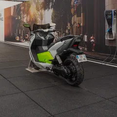 Elektroroller und E-Auto auf stoßdämpfenden WARCO-Platten; verdeckte Reißverschlussverzahnung; Farbton Anthrazit erinnert an Asphalt; temporäre Eventfläche mit Ladepunkt.