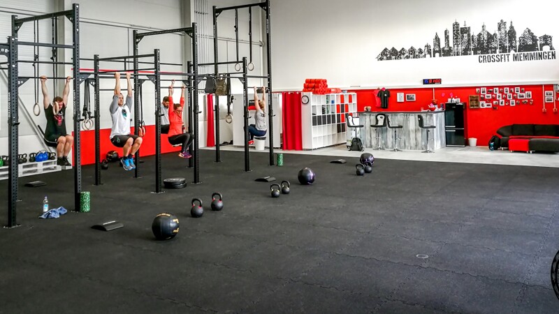 In der Halle der CrossFit-Box in Memmingen trainieren Sportler an der Calisthenics workout Station. Auf den schwarzen Bodenschutzmatten von WARCO, mit denen die CrossFit-Halle ausgelegt ist, liegen einige Kettlebells. Im Hintergrund befindet sich die Umkleide und die Bar.