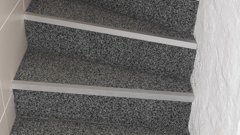 Graue Treppe, die sich im Innbereich von einem Stock zum anderen zieht. Metallschutz an den Kanten.