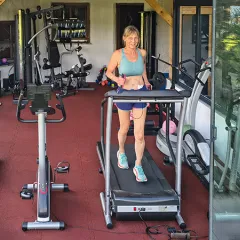 Modernes Homegym mit Glasfront: Eine Frau trainiert auf dem Laufband, der elastische WARCO Fitnessboden schützt Gelenke, dämpft Geräusche und bietet rutschfeste Trittsicherheit – ideal für intensives Training mit Geräten oder Hanteln im privaten Studio.