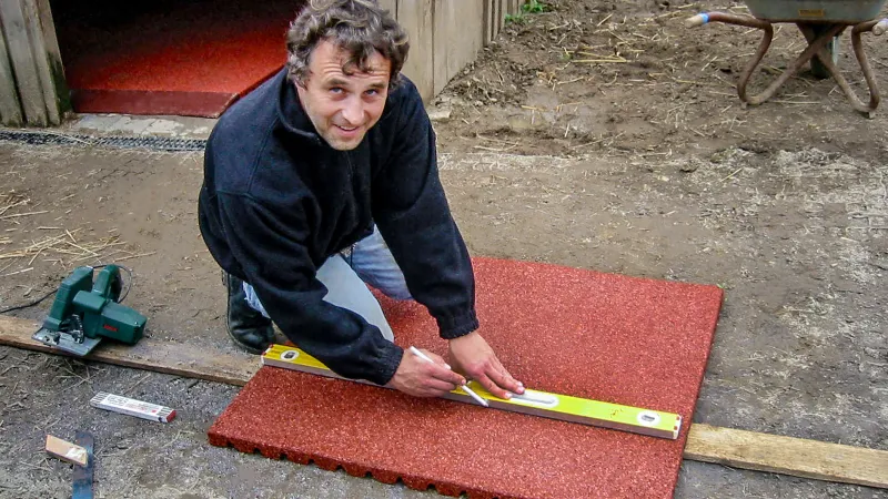 Damit der Schnitt an der richtigen Stelle sitzt, sollte die Schnittlinie auf der Fallschutzmatte oder der Stallmatte vor dem Ansetzen der Säge genau ausgemessen und markiert werden. Eine Wasserwaage und ein Kreidestift sind hilfreich.