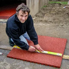 Damit der Schnitt an der richtigen Stelle sitzt, sollte die Schnittlinie auf der Fallschutzmatte oder der Stallmatte vor dem Ansetzen der Säge genau ausgemessen und markiert werden. Eine Wasserwaage und ein Kreidestift sind hilfreich.